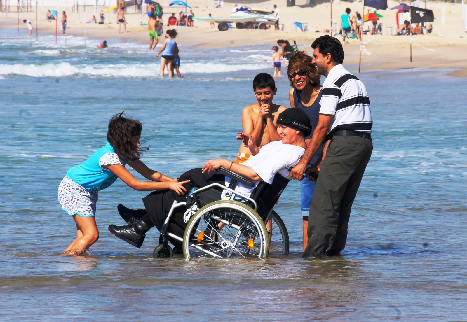 Family helping a wheelchair user into the shallow sea at a beach